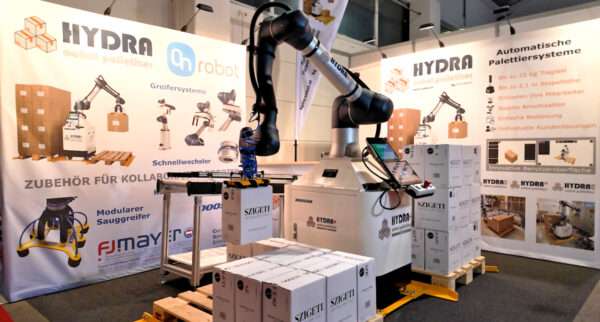 Hydra hebt Weinkarton auf dem Messestand